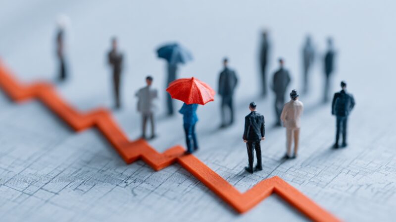 Miniature people standing around a downward graph line, with one figure under a red umbrella representing insurance protection and shared risk