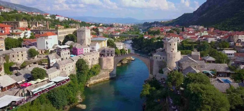 Aerial view of Mostar with Stari Most bridge, stone buildings, red roofs, and the Neretva River.